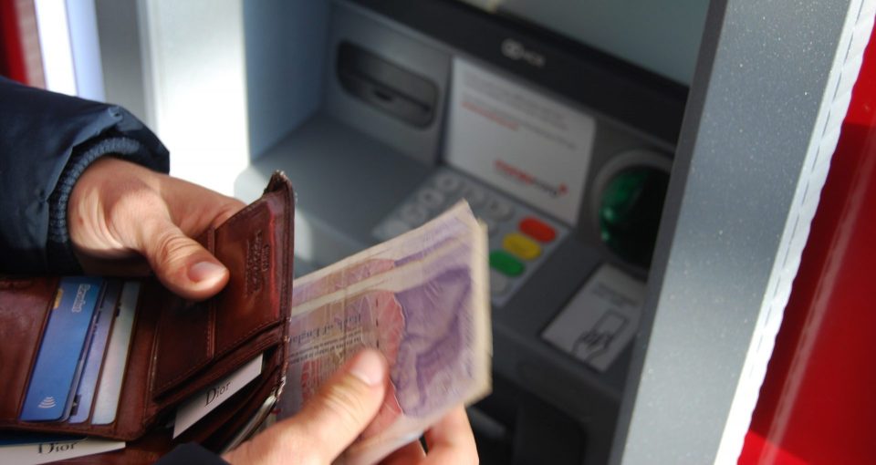 Man withdraws cash from a cash machine and puts it into his wallet.