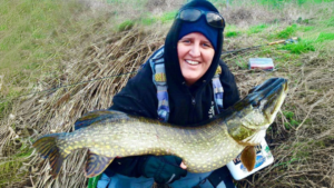 Barbara proudly holds a large pike after catching it on the fly at her local angling venue.