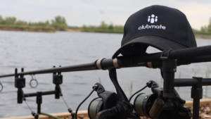 A Clubmate baseball cap sits on top of some fishing rods while their team gets ready to catch some carp at Embryo Habitats’ Baston Shallow venue.