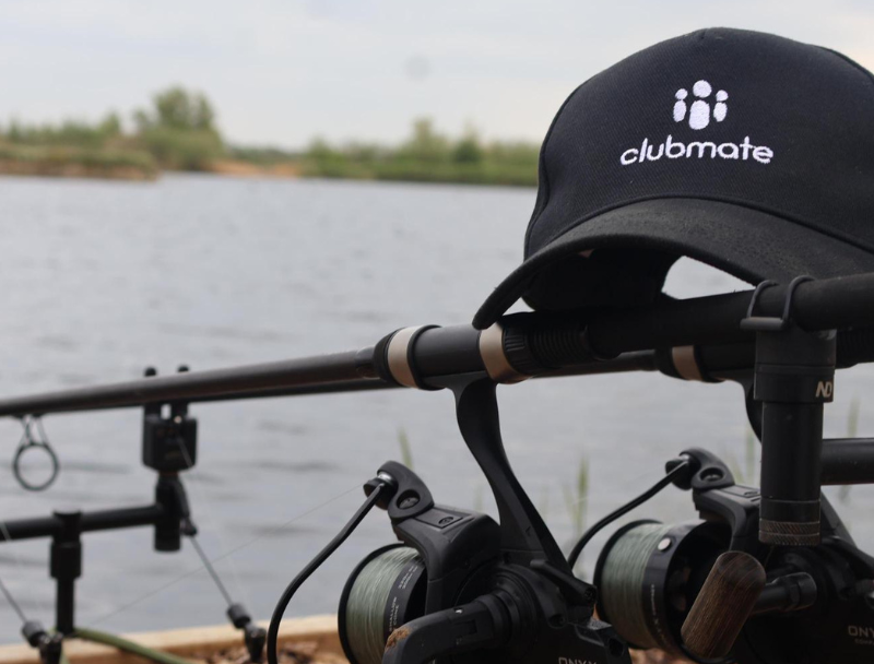 A Clubmate baseball cap sits on top of some fishing rods while their team gets ready to catch some carp at Embryo Habitats’ Baston Shallow venue.